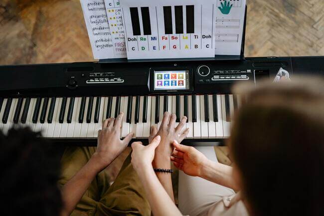 teacher and student are practicing from a piano book with letter notes