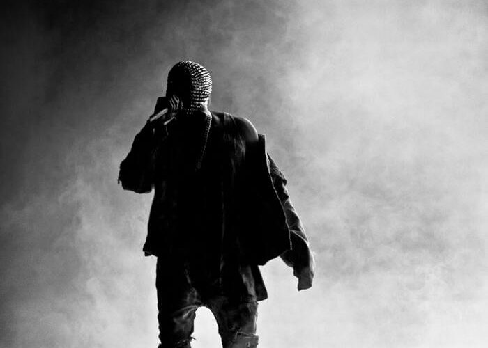 kanye west performing on stage in front of a grey hazy background